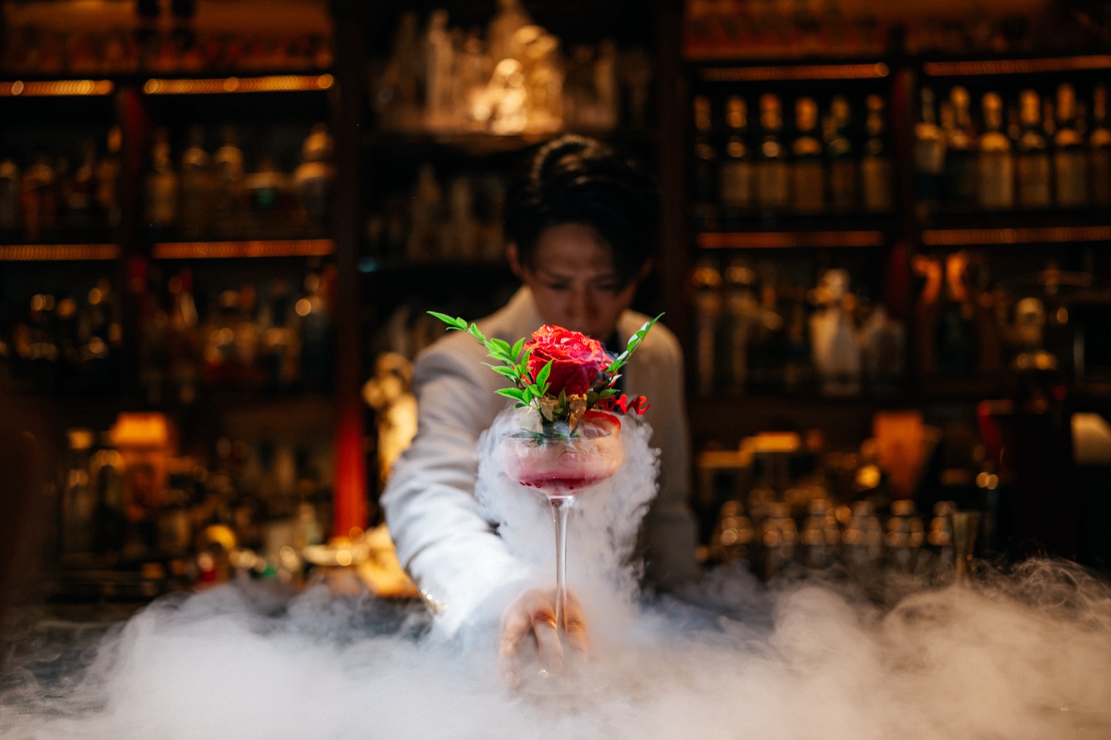 A bartender presenting a smoking coupe crowned with a rose